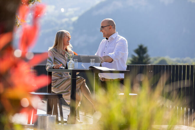 Zwei Inhaus MItarbeiter genießen ein entspanntes Gespräch an einem Tisch im Freien mit malerischem Bergpanorama im Hintergrund. Zwei Inhaus MItarbeiter genießen ein entspanntes Gespräch an einem Tisch im Freien mit malerischem Bergpanorama im Hintergrund.